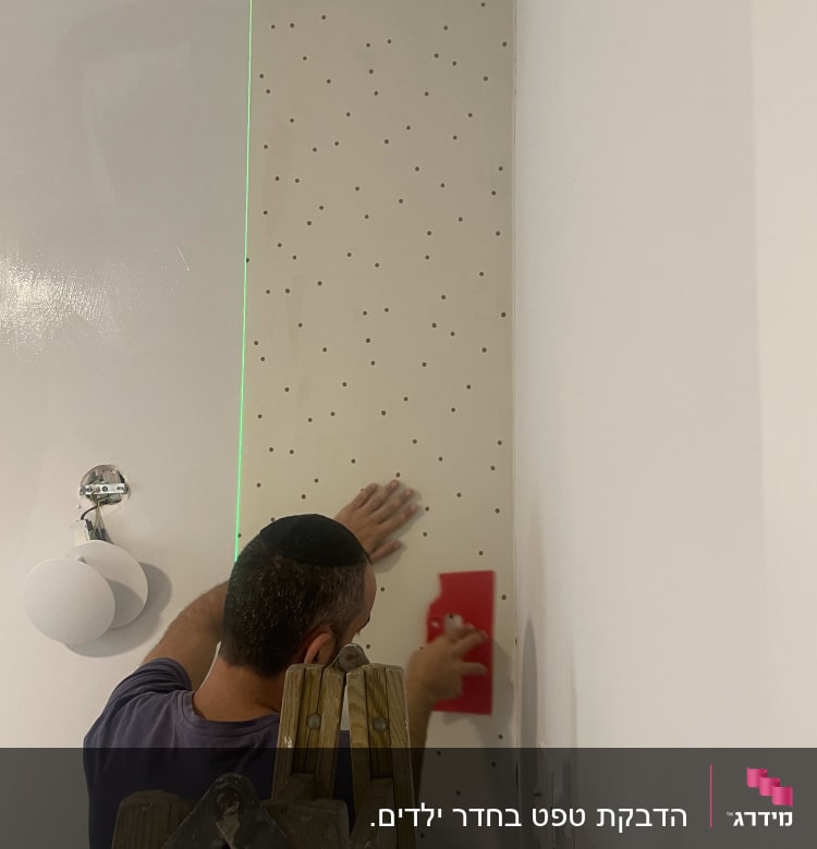 אדם מדביק טפט מנוקד על קיר בעזרת כלי אדום